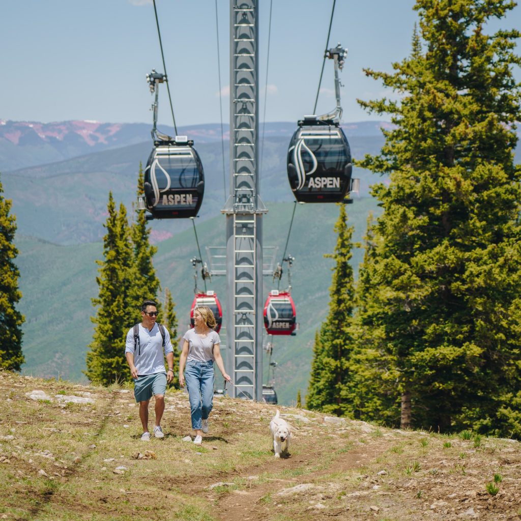 Man and Women on Aspen Mountain hiking to the top under the Aspen Ski Co. Gondolas