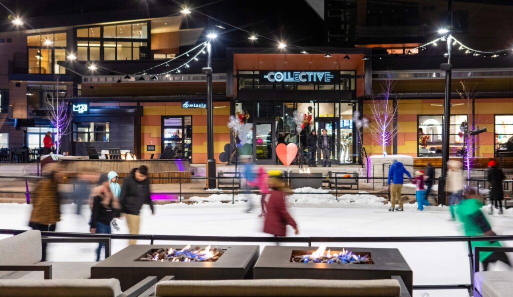People ice skating at night under string lights and next to firepits