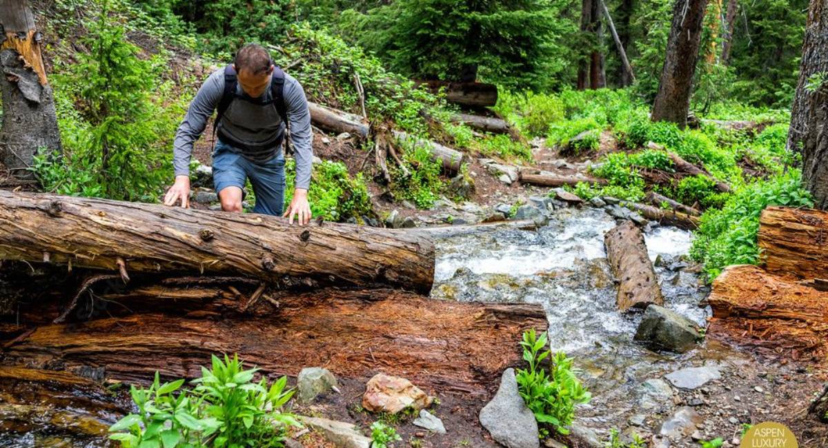 Hiker crossing a creek on a spring trail in Aspen’s green mountain wilderness