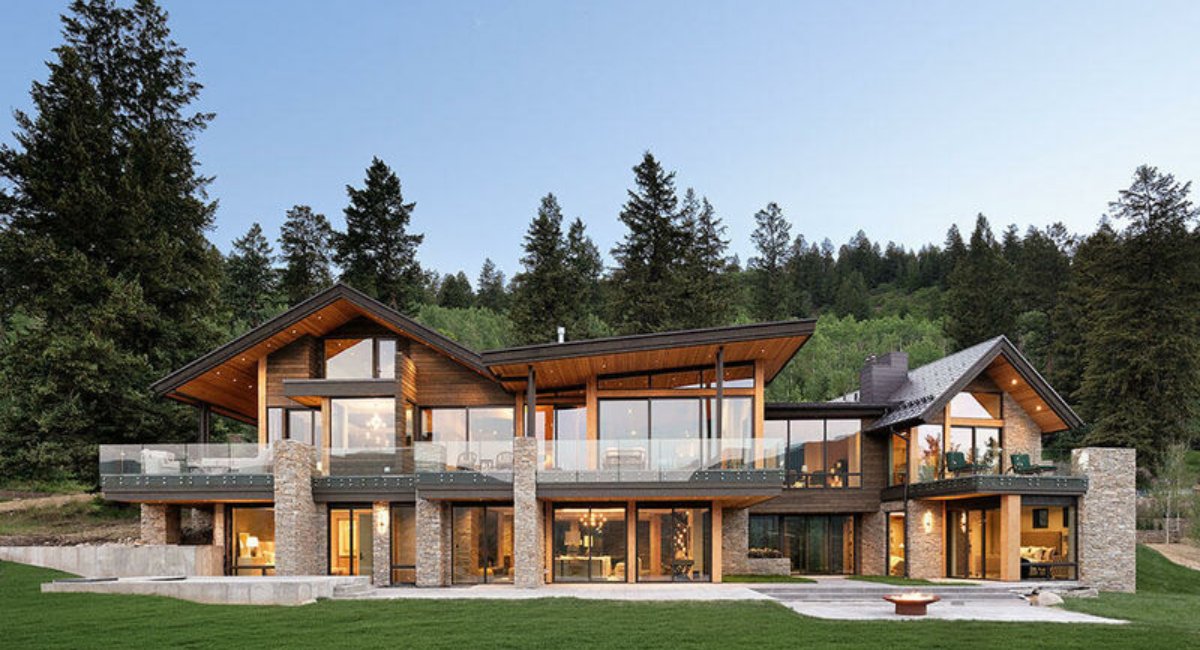 Modern luxury vacation rental in Aspen with warm lighting, set against a backdrop of lush green trees and a clear sky, conveying a peaceful and luxurious ambiance.