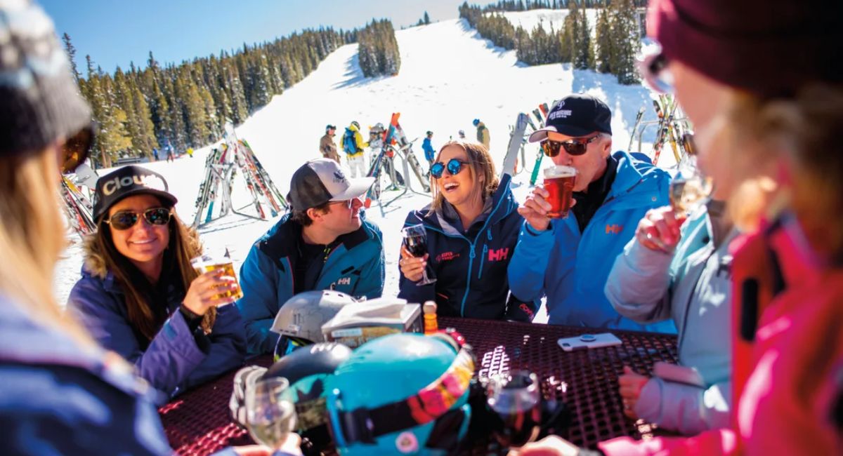 Friends enjoy spring skiing and drinks on a sunny mountain patio in Aspen.