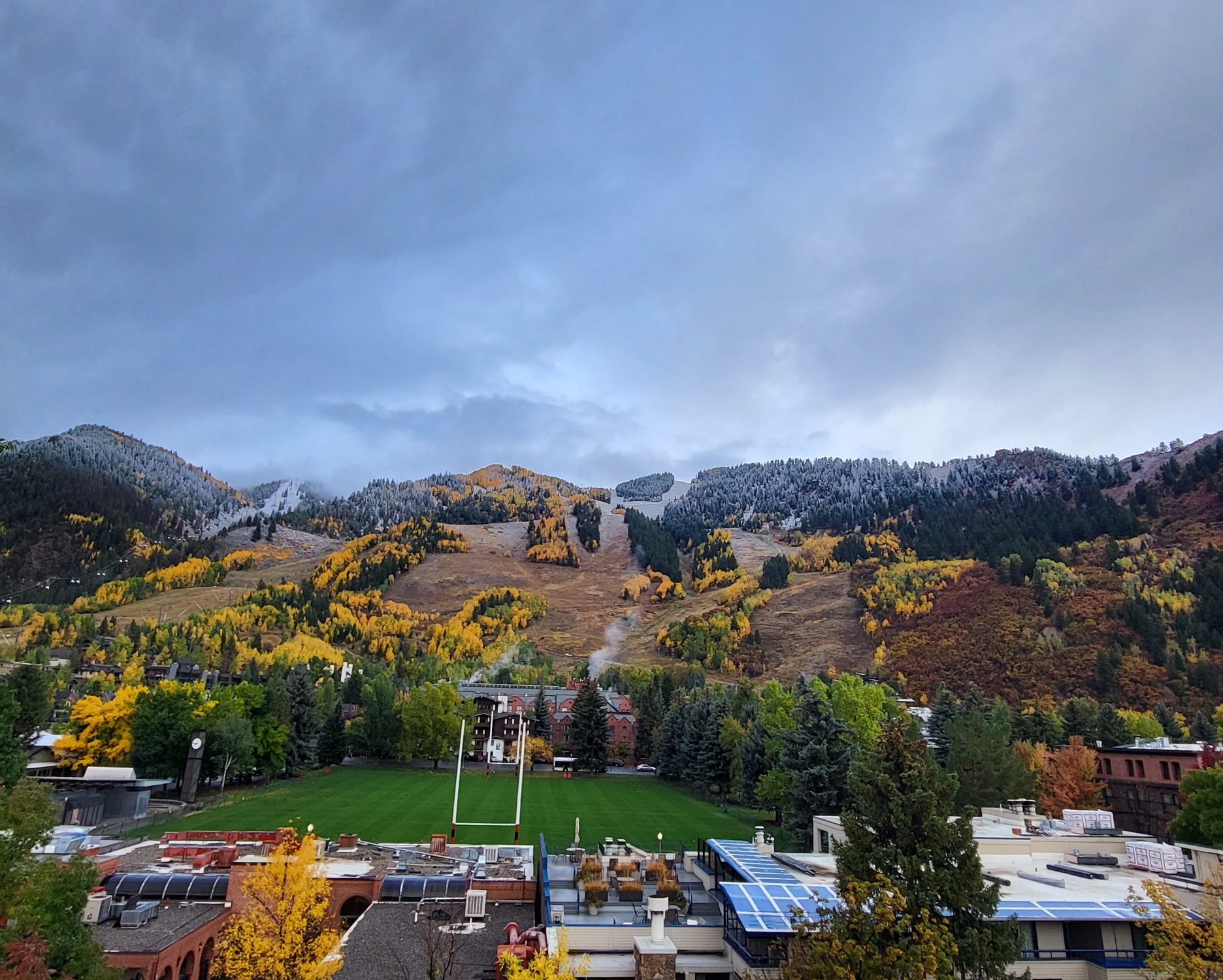 Wide-angle view of a mountain valley in Aspen Colorado with massive groves of golden fall foliage and the first dusting of snow on the peaks during the shoulder season